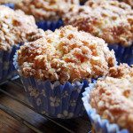Rhubarb muffins with a crumble topping are shown in blue and white paper cases and sitting on a wire cooling rack.