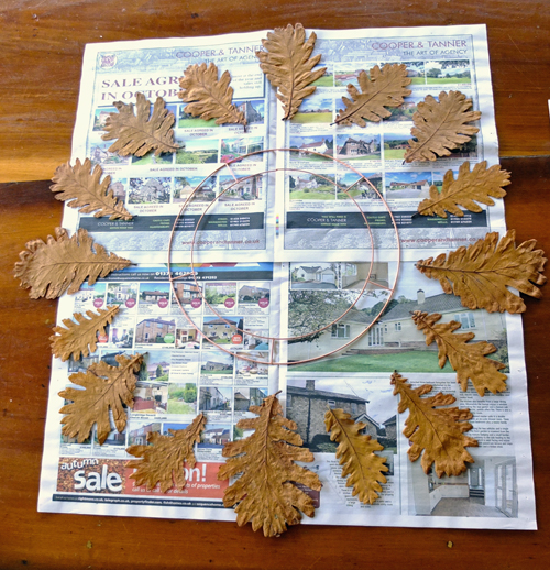 Oak leaves and a copper ring sitting on newspaper, ready to be made into a wreath.