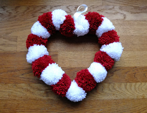 Valentine's day heart-shaped Pom Pom Wreath on a wooden floor.