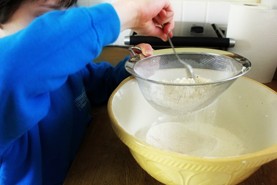 Sifting flour through a sieve into a bowl.