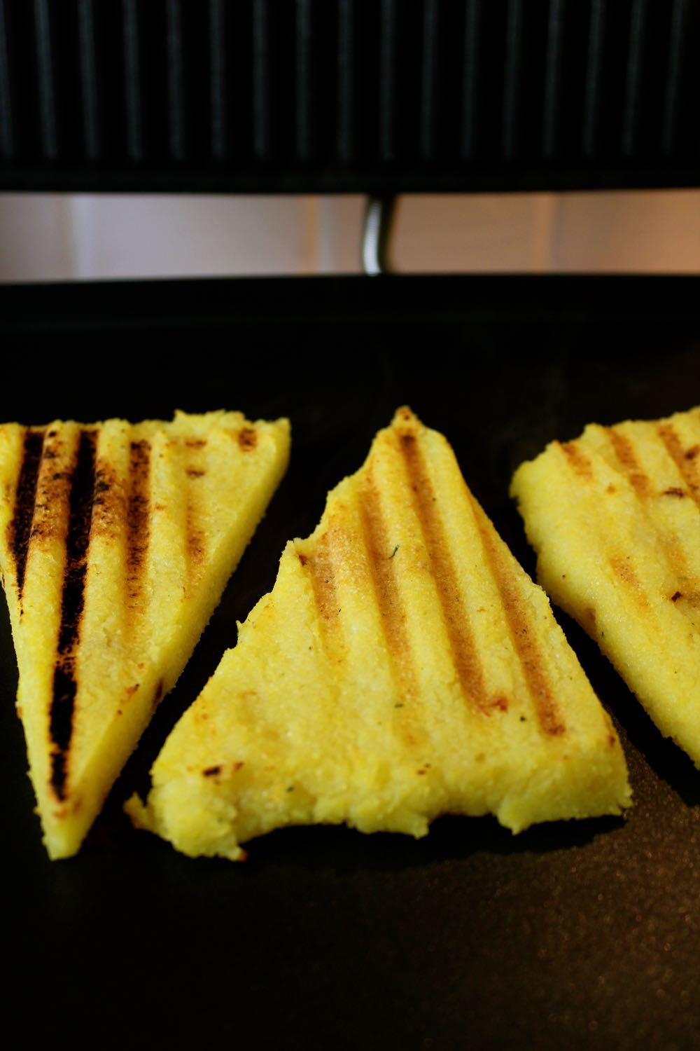 Three pieces of Griddled Polenta Bruschetta on the grill.