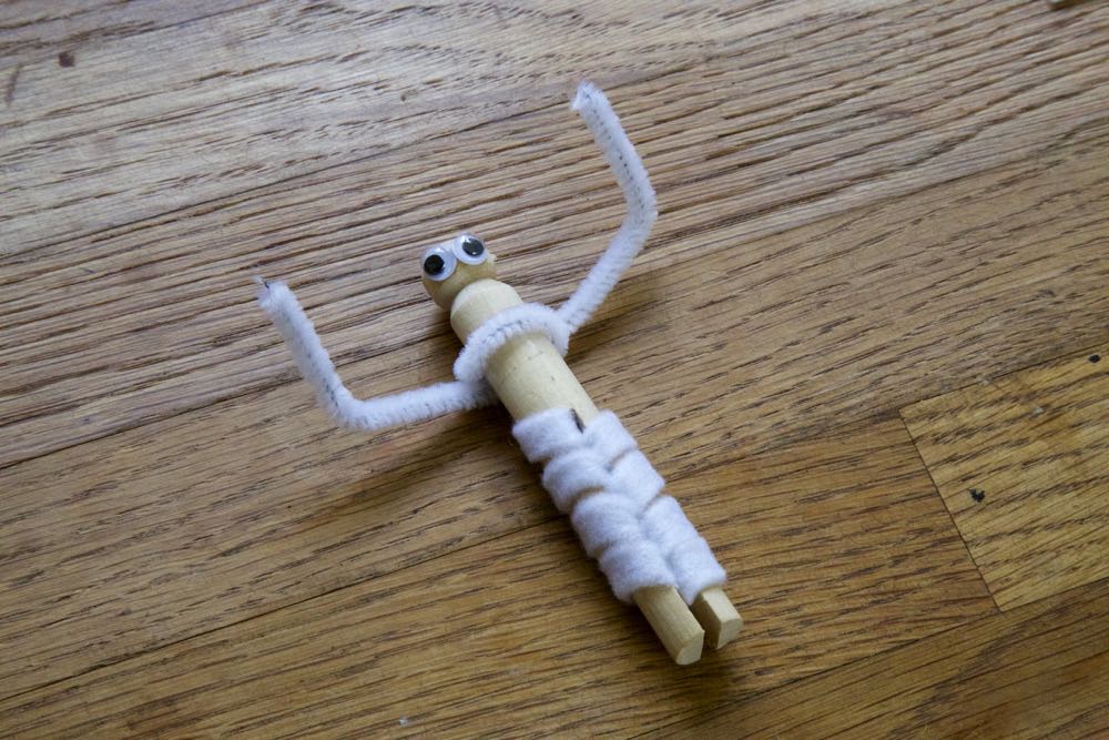 Clothes peg with pipe cleaner arms, googly eyes and the beginning of the bandage wrapping.