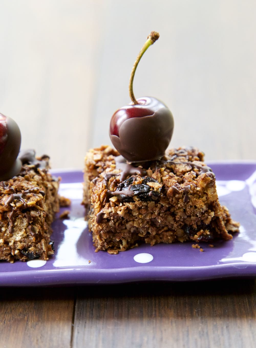 Chocolate Flapjack topped with a chocolate coated fresh cherry sitting on a purple polka dot serving tray.