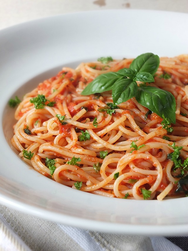 Chilli Spaghetti topped with basil leaves, served on a white plate.