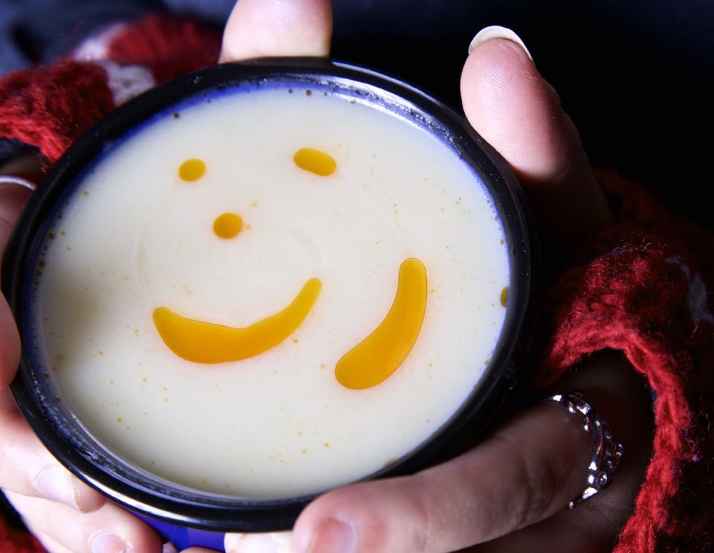 Celeriac Soup in a mug with a swirl of chilli oil held in gloved hands.
