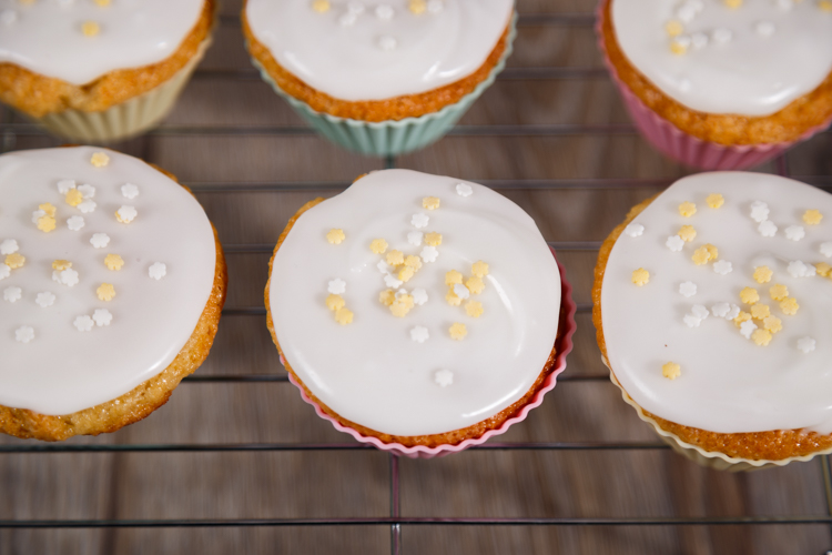 Glace icing topped with pastel star sprinkles on lemon cupcakes sitting on a wire cooling rack.