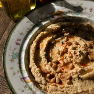 A bowl of chickpea hummus topped with pine nuts, paprika and thyme.