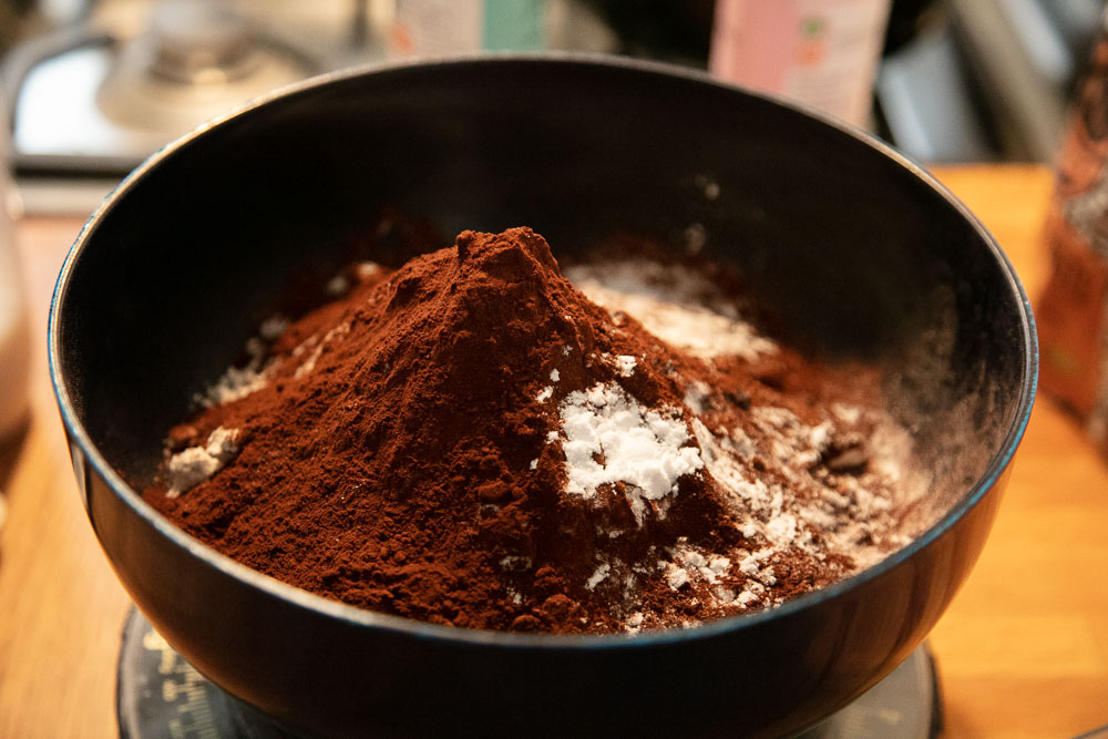 Cocoa, self raising flour and baking powder on measuring scales.