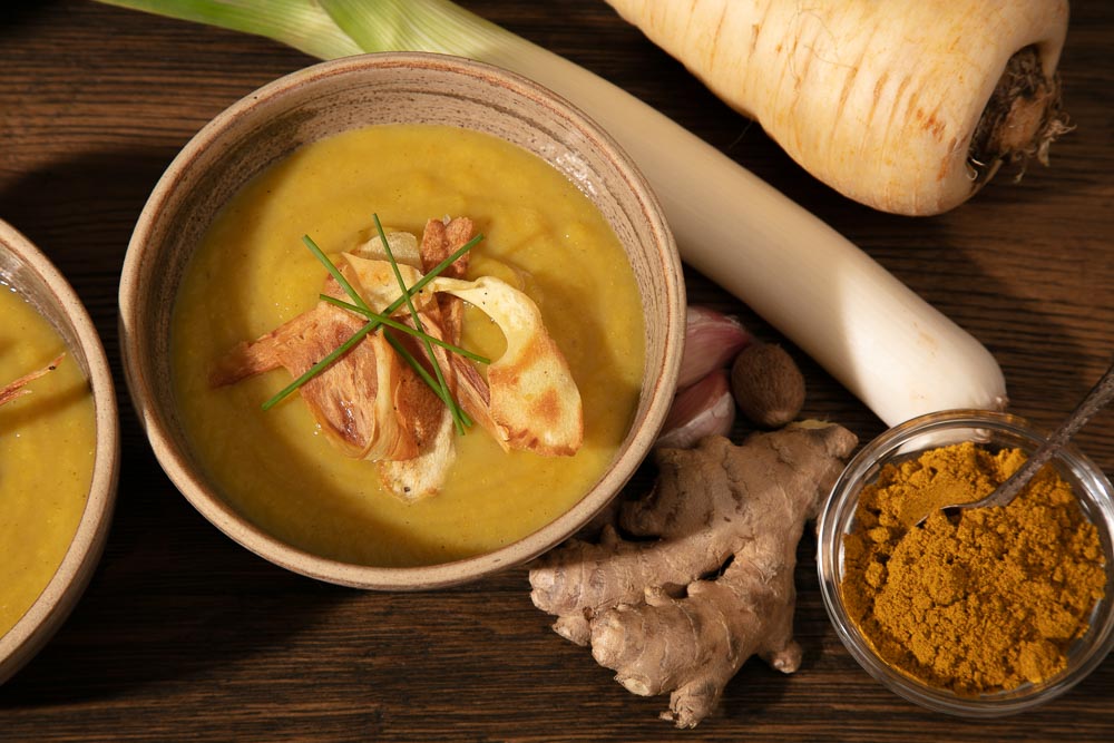 A bowl of vegan parsnip soup alongside the ingredients to make it.