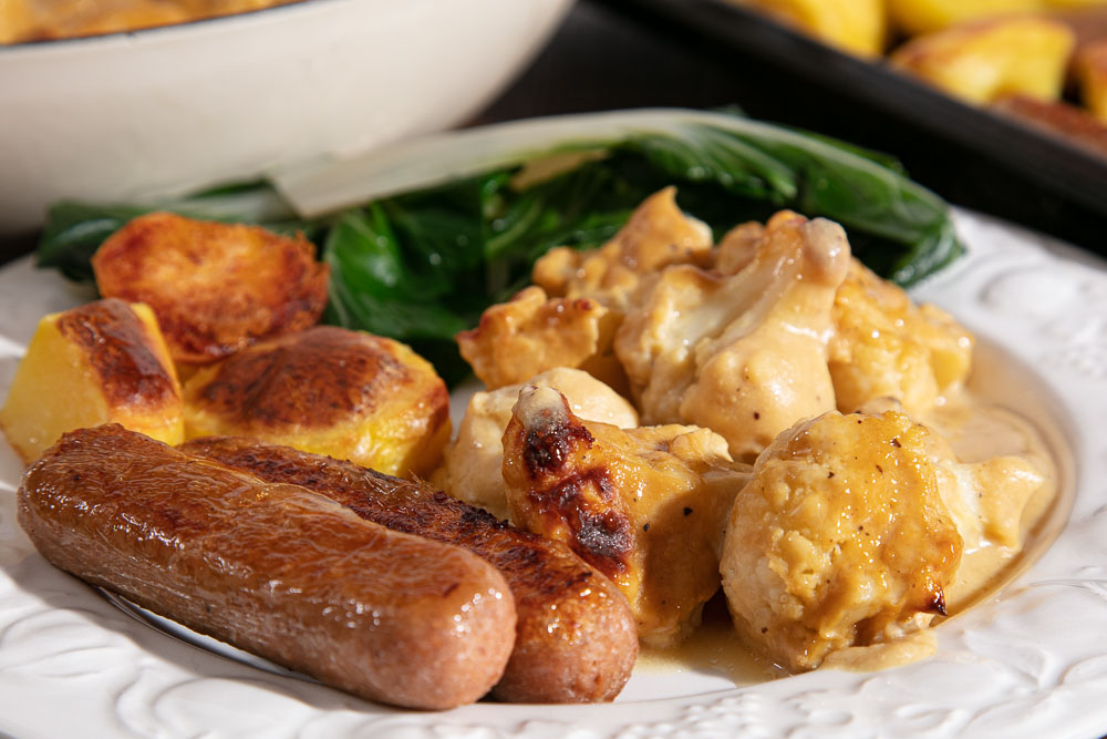 Vegan cauliflower cheese served with sausages, roast potatoes and swiss chard.