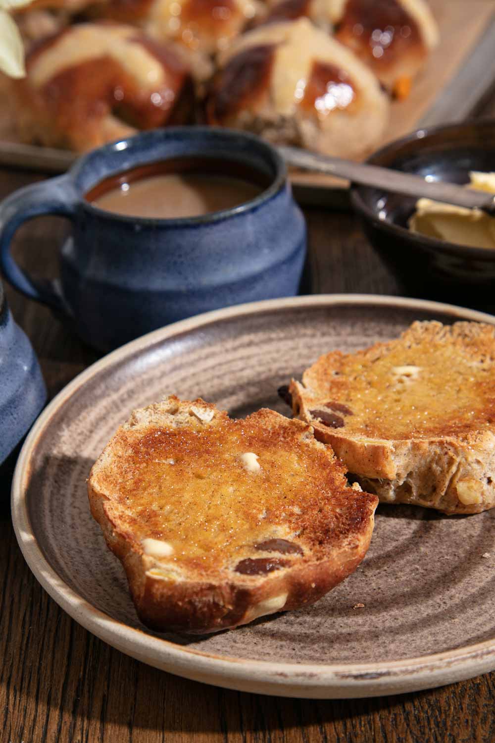 Toasted vegan hot cross bun spread with butter. Served with a cup of tea.