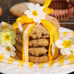 A stack of vegan Easter biscuits tied with yellow ribbons and topped with fresh primrose flowers.