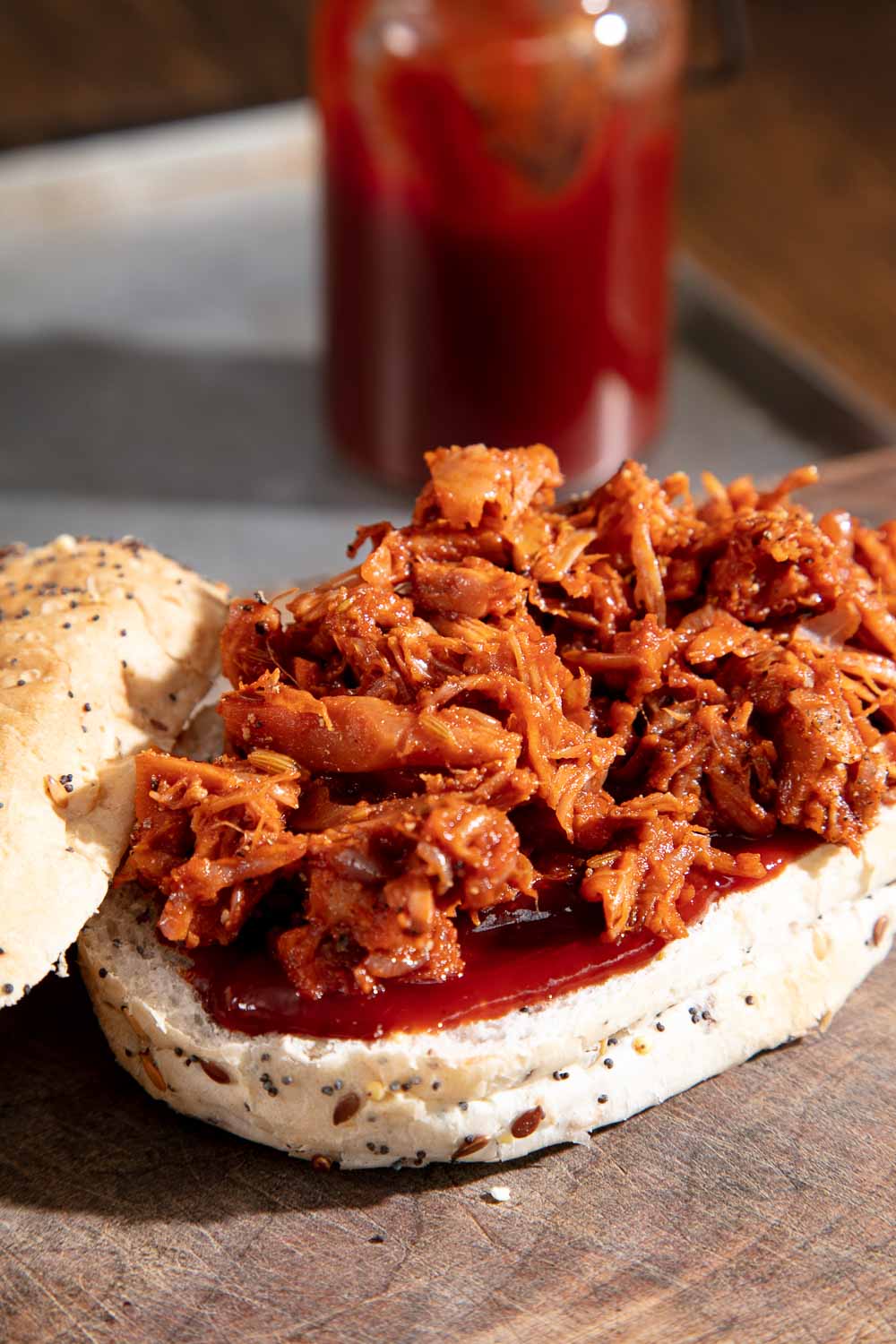A layer of BBQ sauce on a bun base with jackfruit piled on top. 