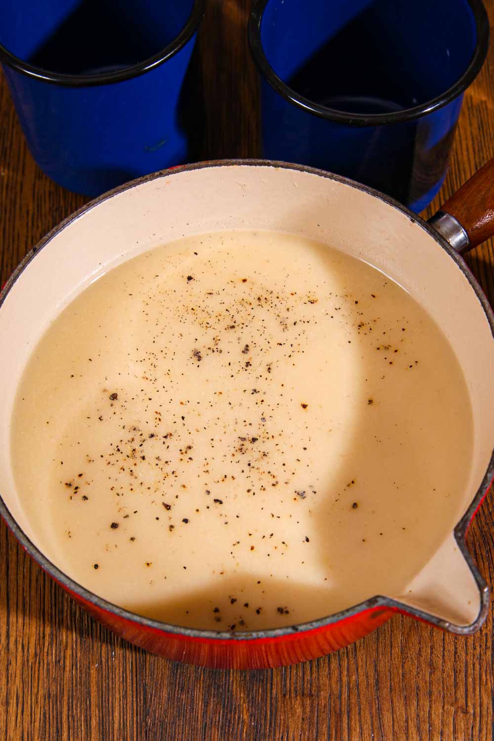 An enamel pan full of onion soup. The soup has ground pepper on top and the light is casting a shadow that creates a heart shape on the surface of the soup.