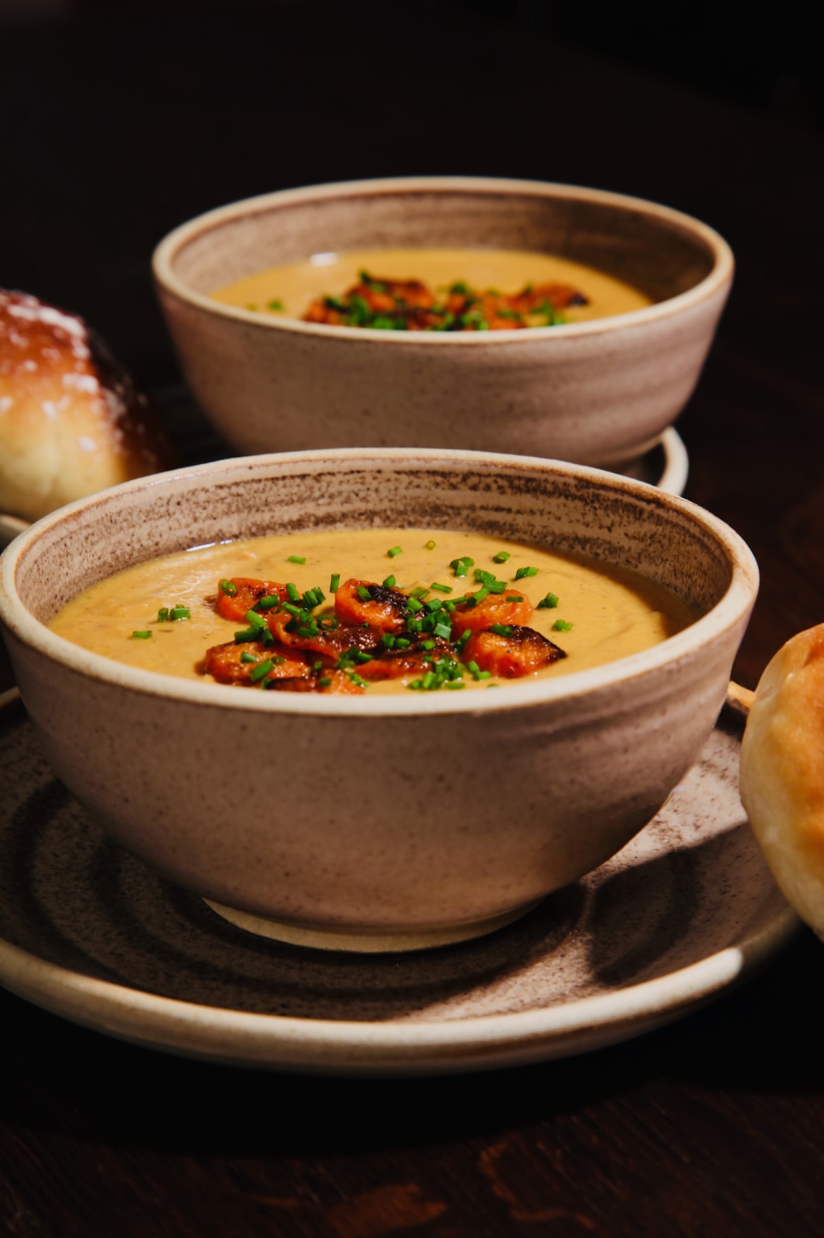 Two bowls of roasted carrot soup topped with sliced roasted carrots and chopped green chives.