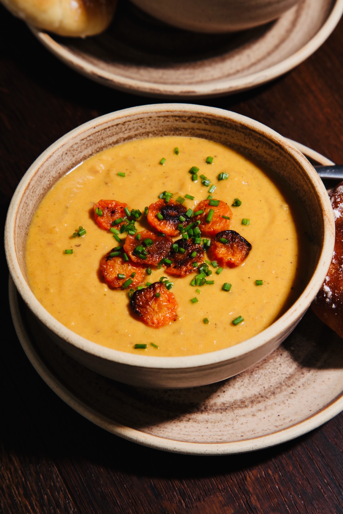 A bowl of spiced roasted carrot soup topped with chopped chives and roasty carrot slices. 