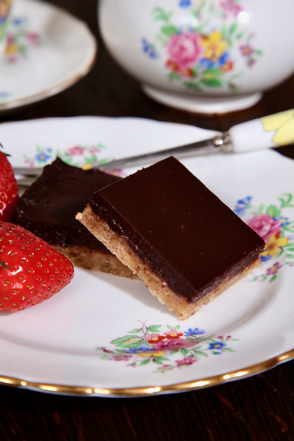 Two chocolate pecan bars sitting on a pretty floral side plate. A matching jug and tea cup can just be glimpsed in the background.