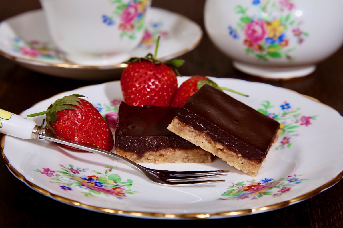 Two vegan chocolate pecan slices sit on a vintage tea plate.