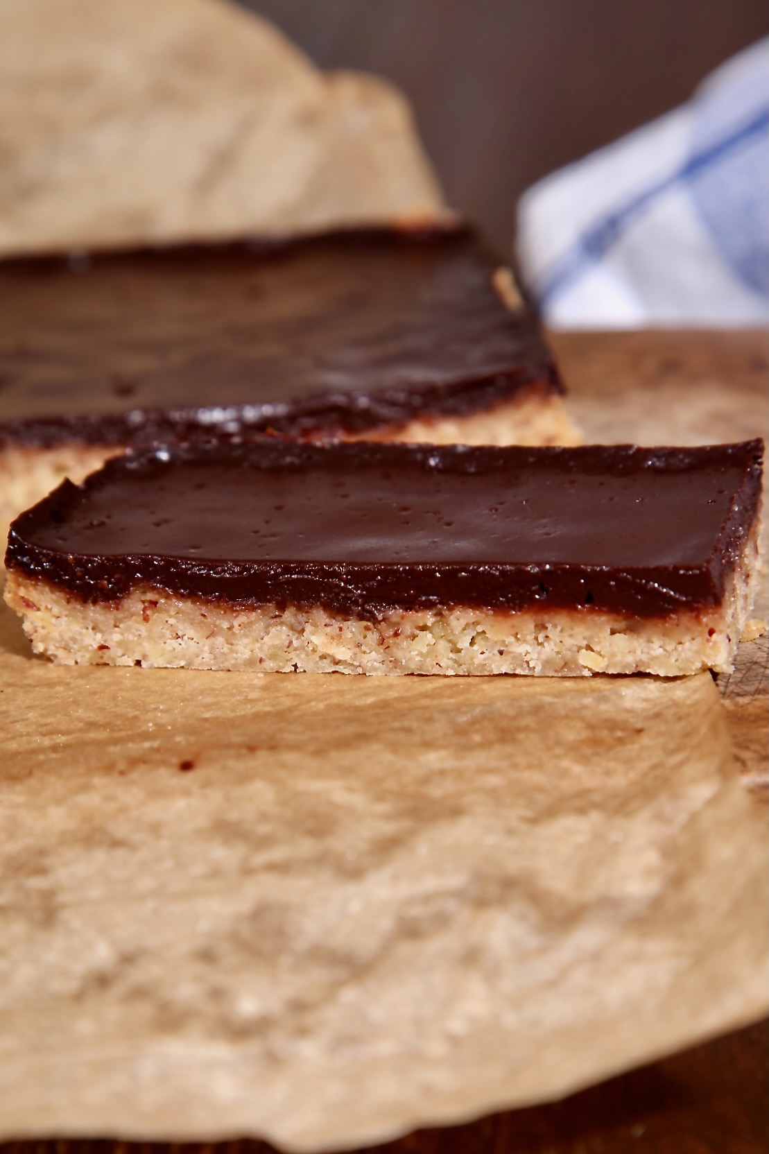 A piece of cleanly sliced chocolate pecan traybake sitting on baking parchment. The rest of the traybake can be seen in the background.