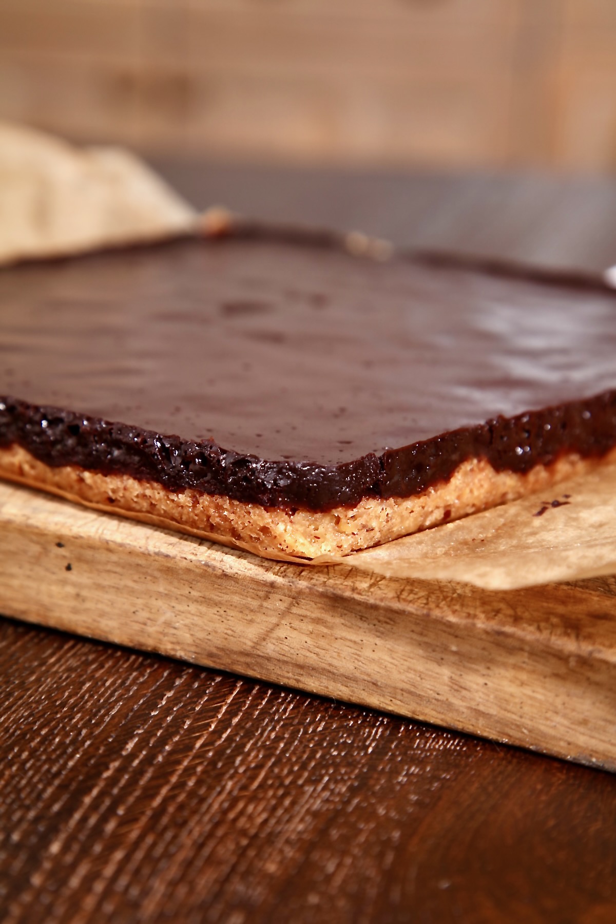 A vegan chocolate pecan traybake, straight from the oven, sitting on baking parchments and a wooden board to cool. 